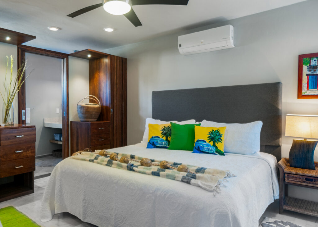Bed with yellow and green tropical cushions beside wooden storage and a bedside lamp.