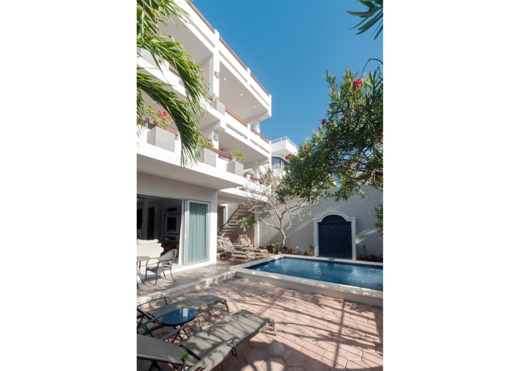 Pool and lounge chairs beside a white multistory building with balconies.