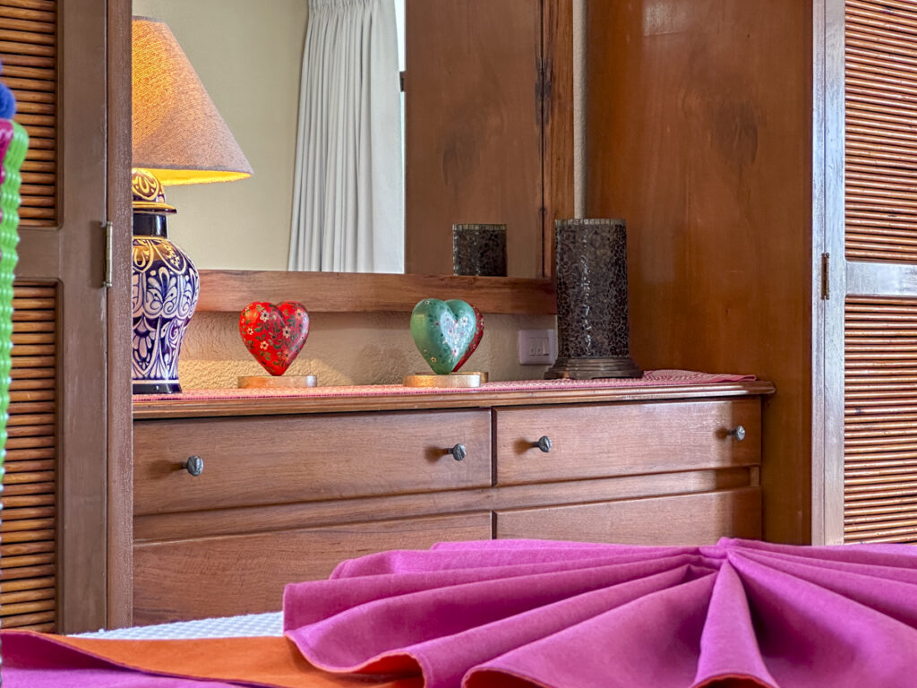 Wooden dresser beneath a large mirror with colorful heart ornaments and a lamp.