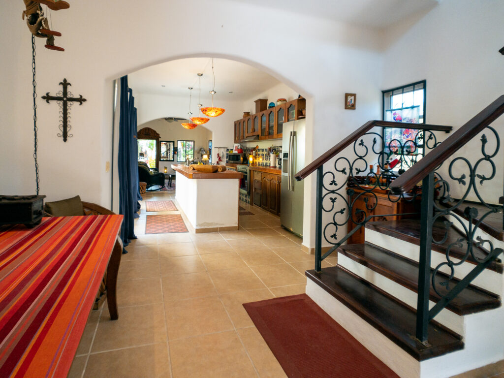 Staircase with ornate black iron railings beside an arched opening to the kitchen.