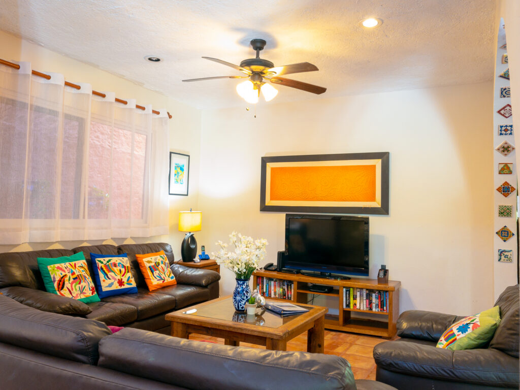 Dark sofas and wooden coffee table face a television beneath orange artwork.