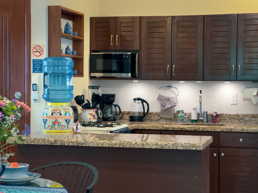 Kitchen with dark wooden cabinets, microwave, coffee maker, kettle, and a stone breakfast counter.