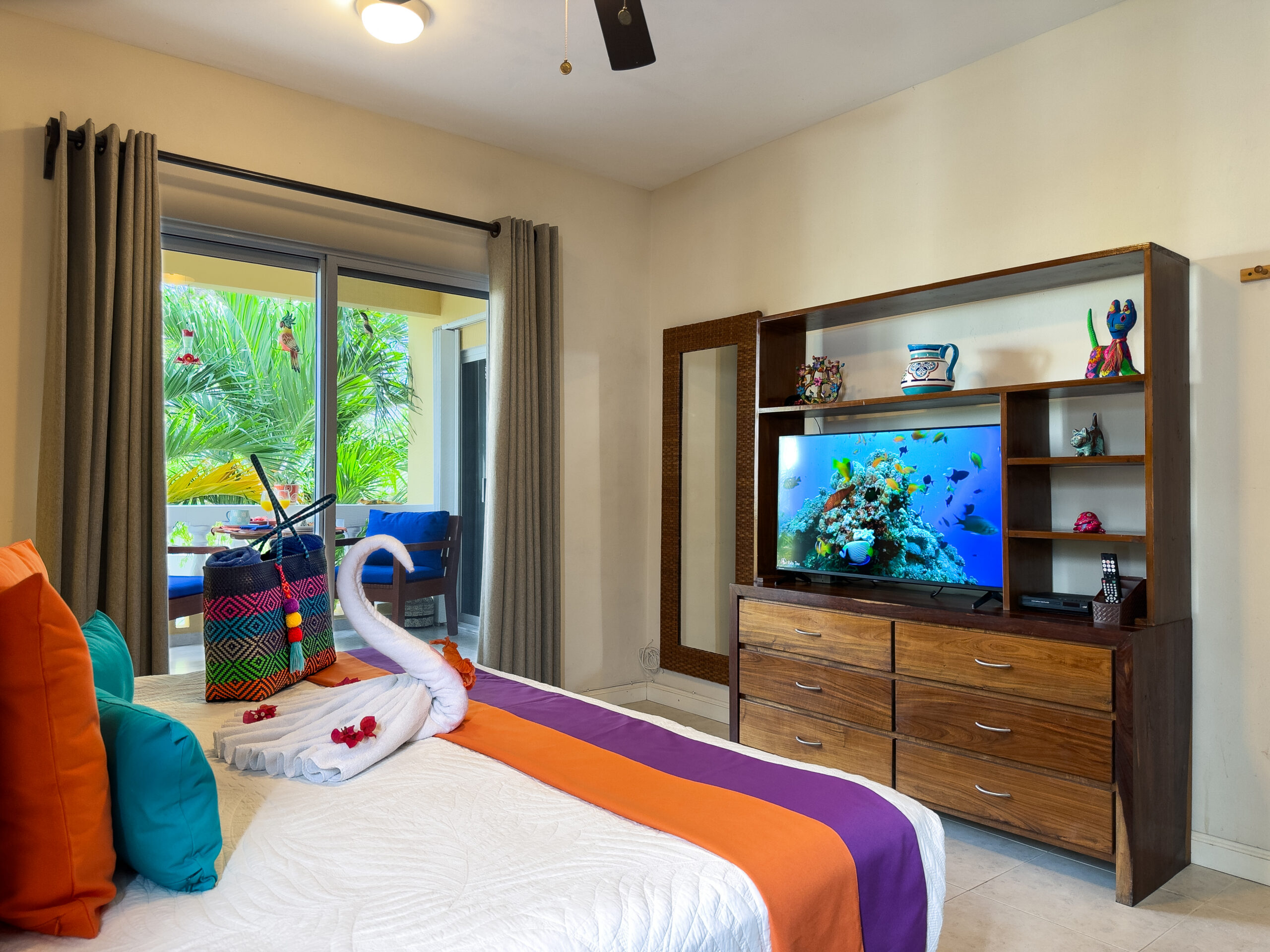 Wooden dresser with television and shelving beside a bed with colorful runners.