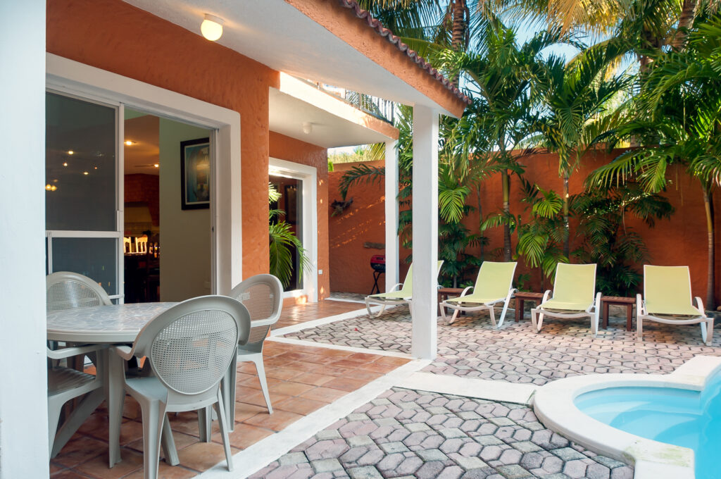 Outdoor table and chairs beneath a covered patio beside the pool and lounge chairs.