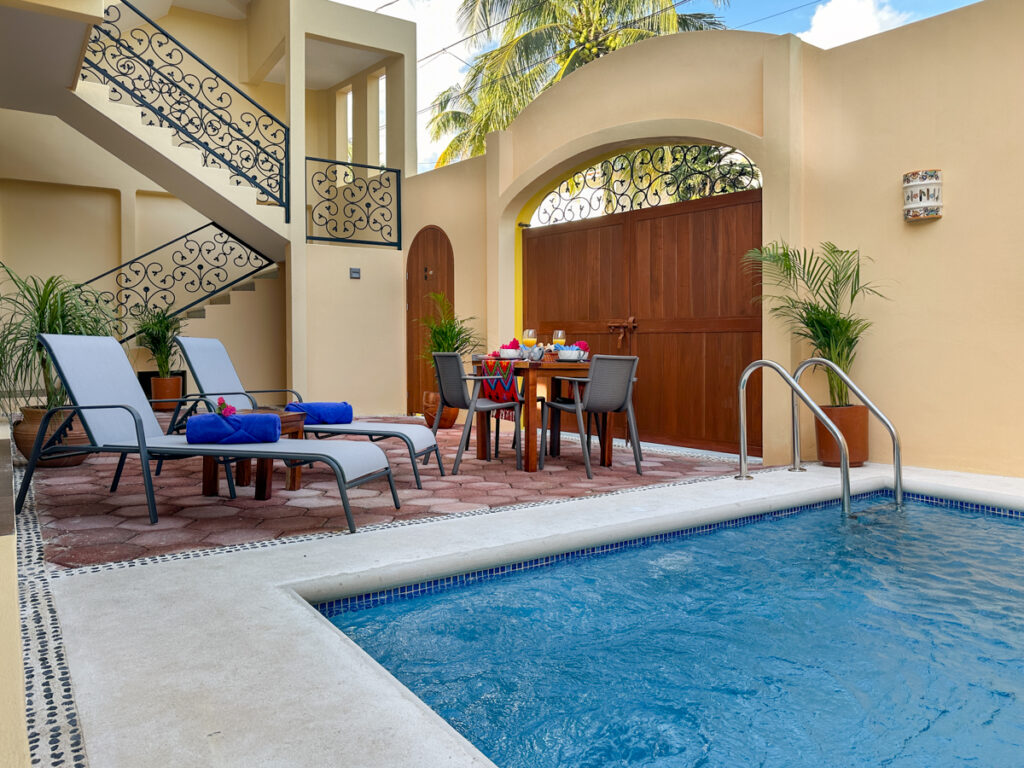 Pool beside reclining chairs and a dining table beneath an arched entrance gate.