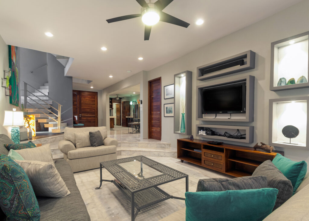 Sofas with turquoise cushions around a glass-topped table facing a wall-mounted television.
