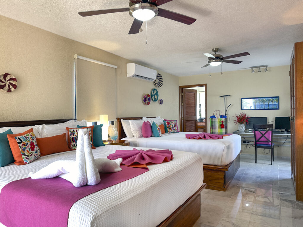 Two beds with pink accents and towel decorations, with a desk at the far end of the room.