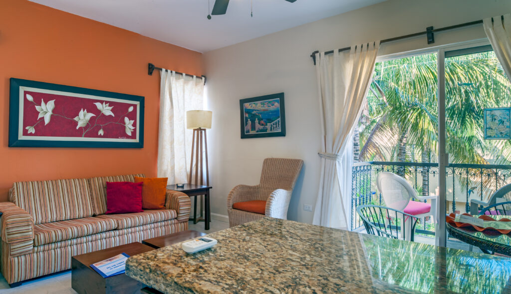Striped sofa and wicker chair beneath an orange accent wall beside sliding doors to the balcony.