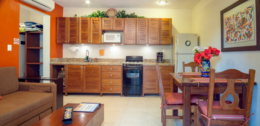 Wooden kitchen cabinets, stove, and microwave behind a living area with a sofa and dining table.