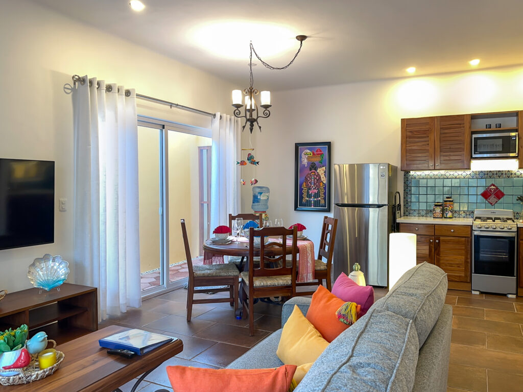 Gray sofa facing a dining table and kitchen with wooden cabinets and stainless steel appliances.