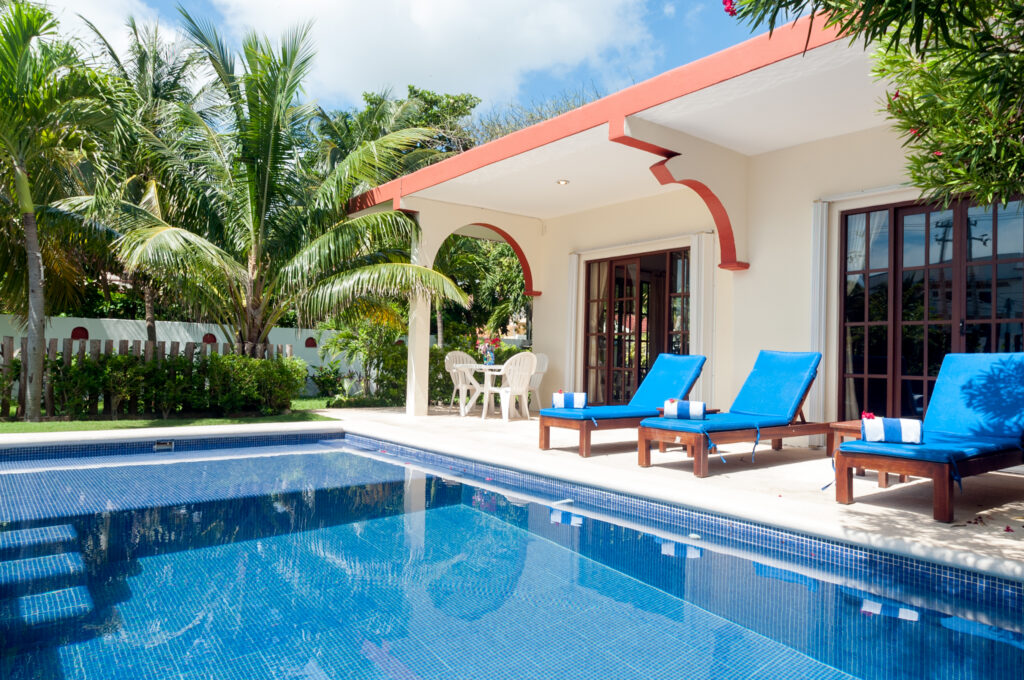 Blue swimming pool beside bright blue lounge chairs in front of the house.