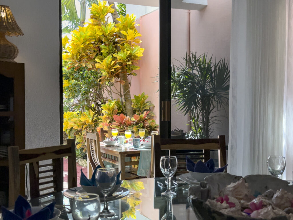 Indoor table with glassware near open doors to an outdoor table among courtyard plants.