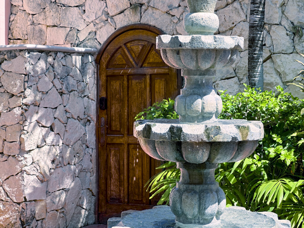 Close view of a stone fountain in front of an arched wooden gate set into a stone wall.