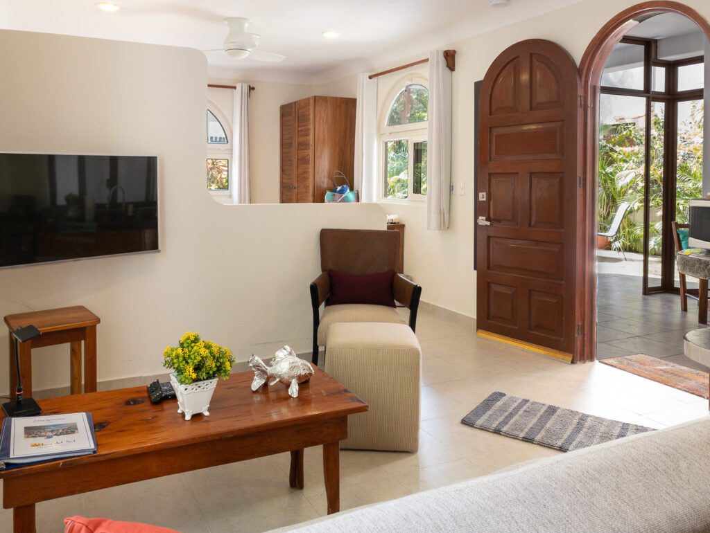 Wall-mounted television, wooden coffee table, and chair with ottoman beside the open entrance.