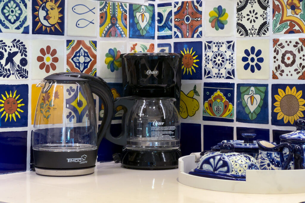 Coffee maker, glass kettle, and blue-and-white dishes on a counter against patterned tiles.