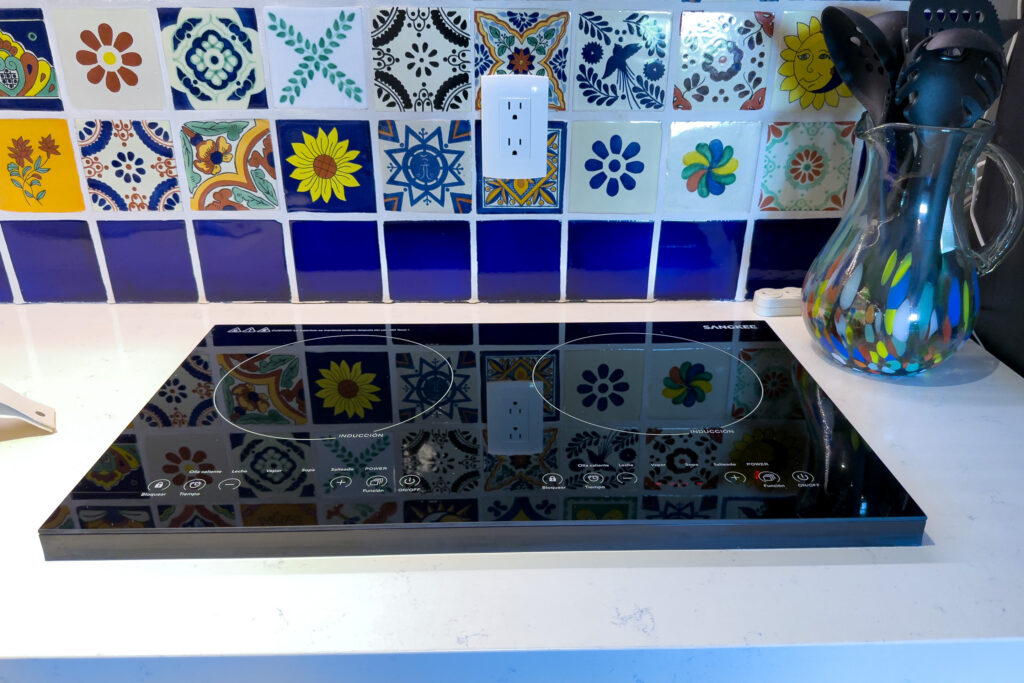 Black glass cooktop set into a white counter beneath a colorful tile backsplash.