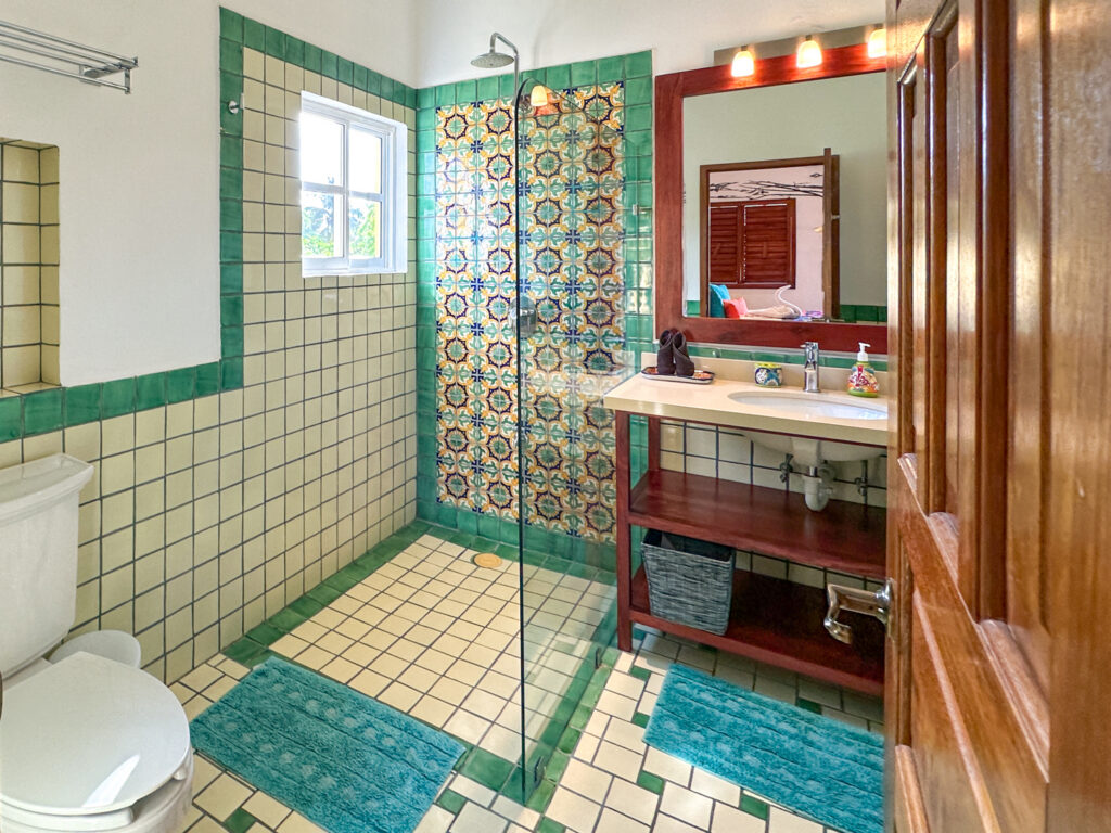 Bathroom with a tiled shower, wooden vanity, mirror, and green tile borders.