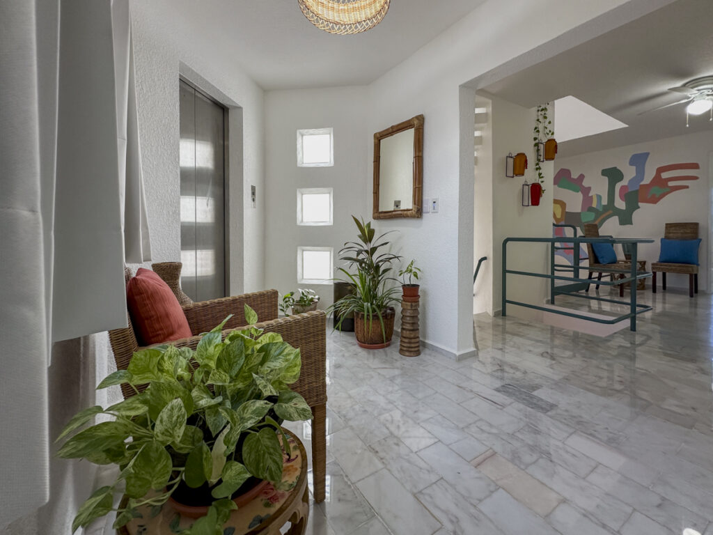 Wicker seating, a potted plant, and a mirror along an upstairs hallway beside the stair railing.