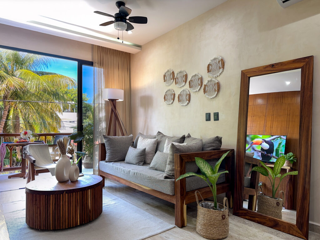 Sofa, round coffee table, tall mirror, and a potted plant beside the balcony.