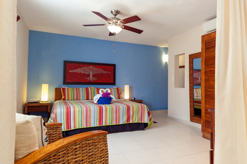 Bed with a striped cover and bedside lamps against a blue wall beneath red artwork.