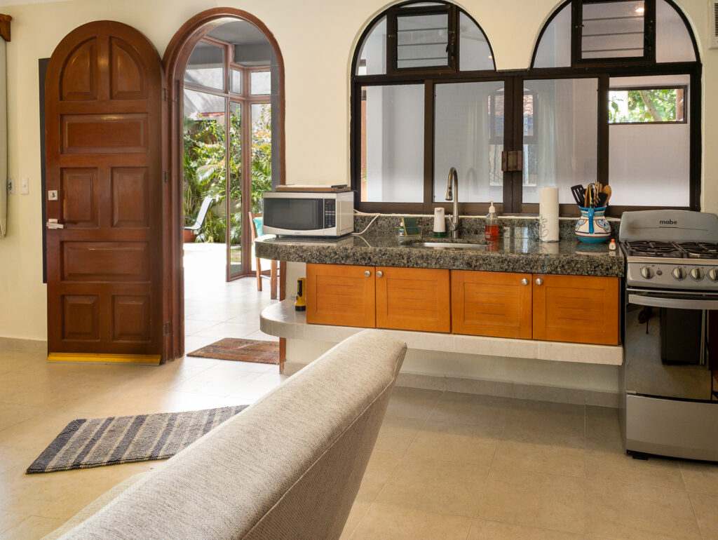 Kitchen sink and stove beneath arched windows beside an open wooden entrance door.