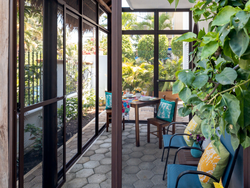 Blue chairs and a dining table along a screened patio beside climbing greenery.
