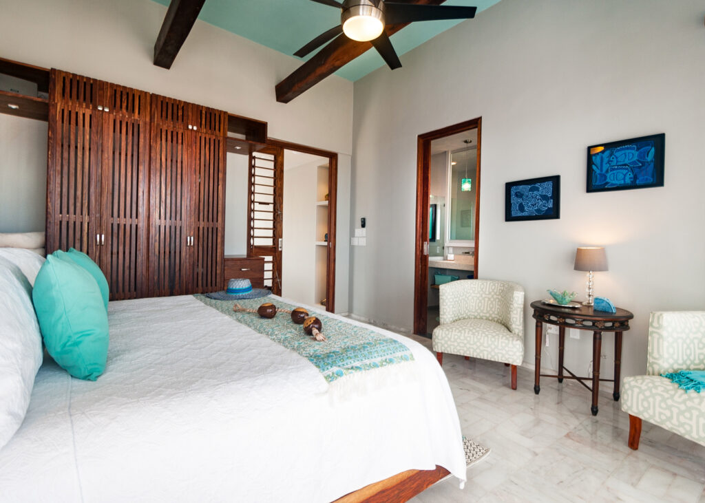 Bed beside wooden storage screens and two upholstered chairs around a small table.