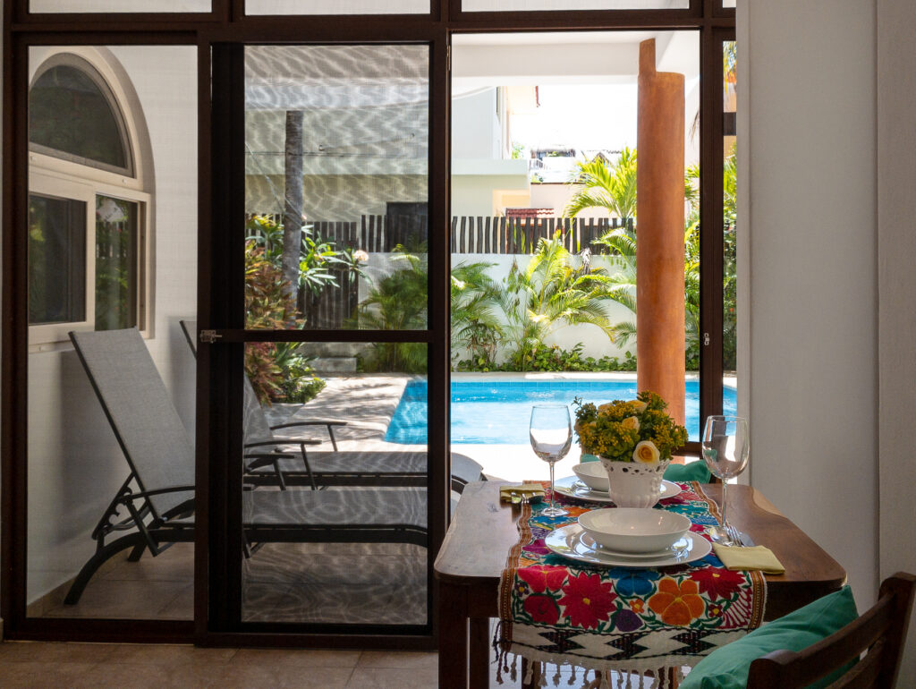 Dining table set with dishes and flowers in an enclosed patio overlooking the pool and lounge chairs.