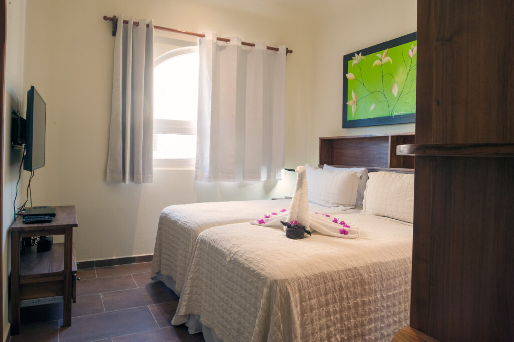 Two beds beneath green floral artwork facing a television beside a curtained window.