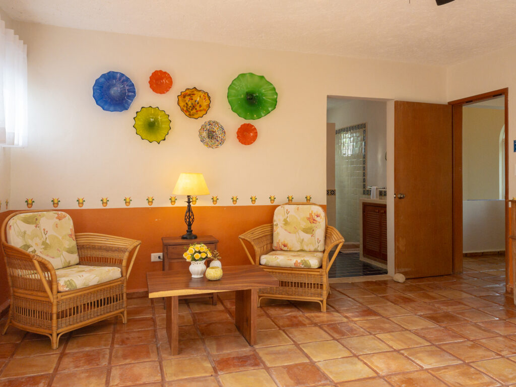 Two wicker chairs and a small wooden table beneath colorful wall plates near a wardrobe.