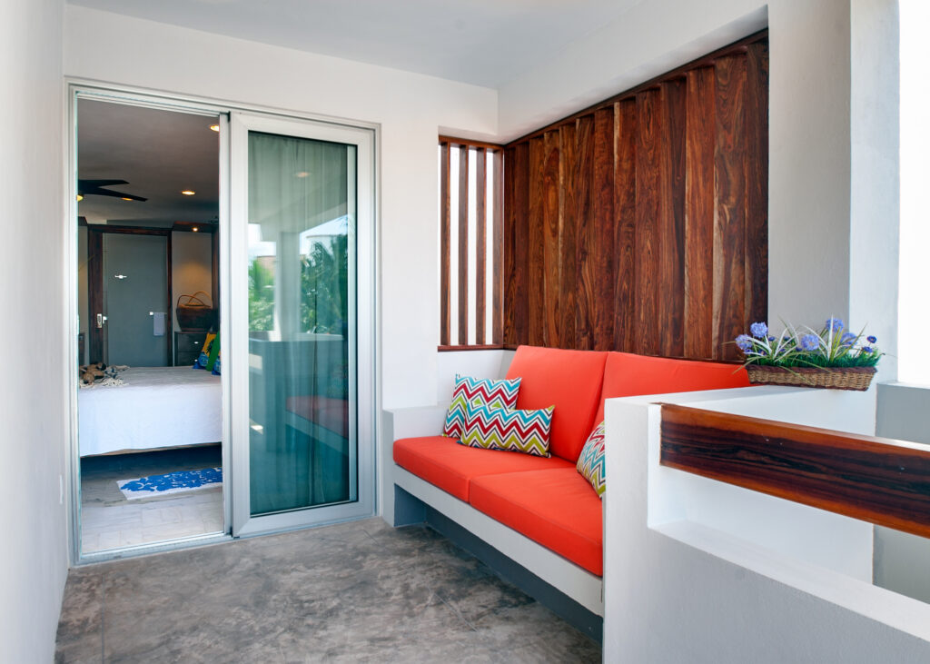 Built-in bench with orange cushions beside a sliding bedroom door and wooden privacy screen.