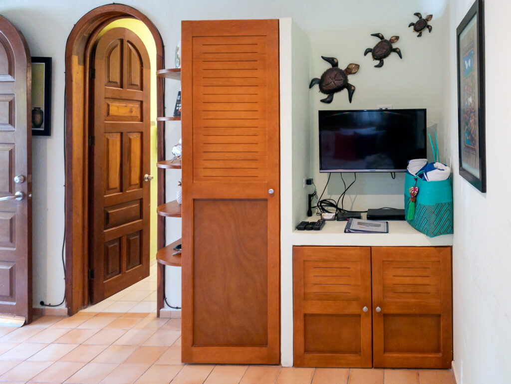 Television above a wooden cabinet beside tall storage and an arched doorway, with turtle wall decorations.
