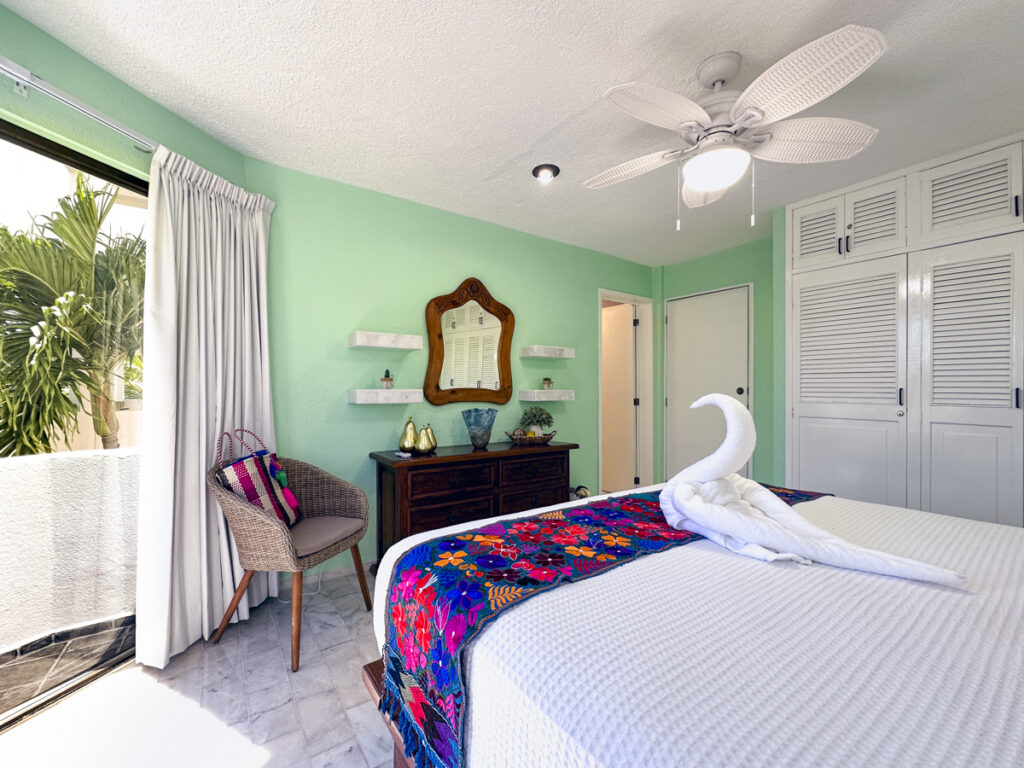 Bed with towel swan beside a wooden dresser, ornate mirror, and white closet doors.