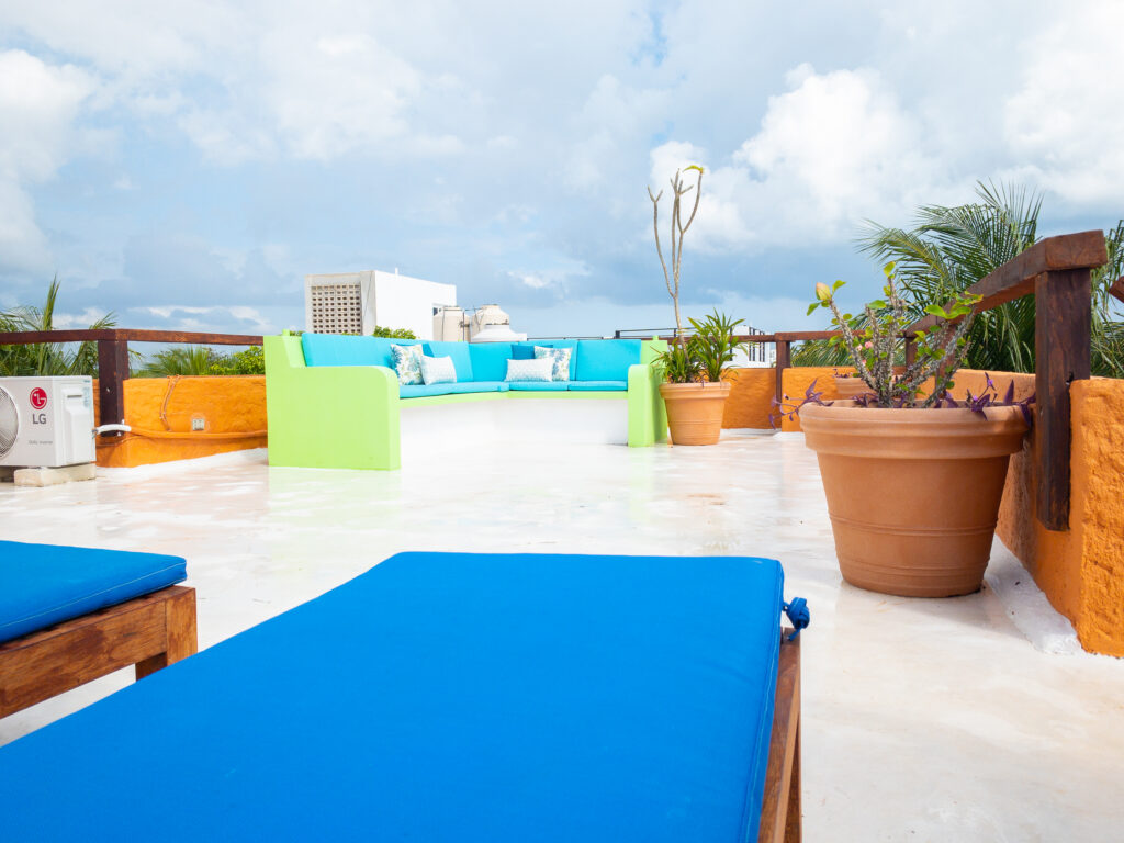 Blue lounge cushions and pale green walls on a rooftop terrace with potted plants.
