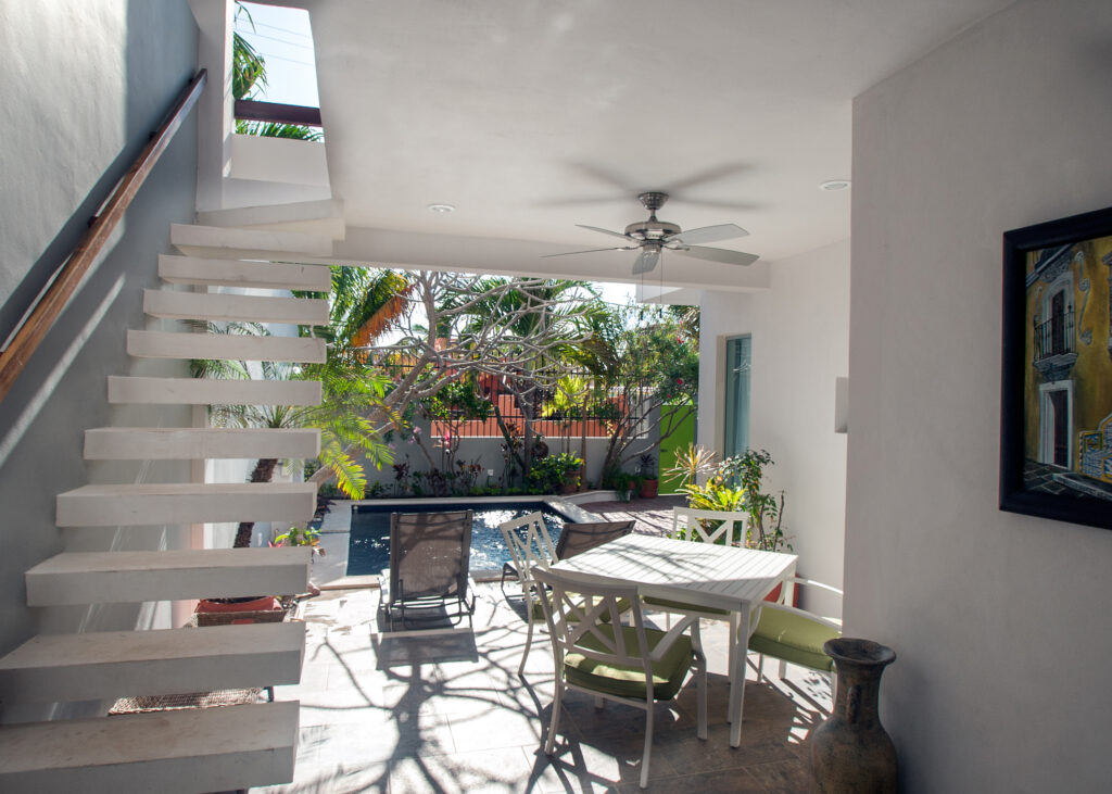 Outdoor dining table and chairs beside an open exterior staircase near the pool.