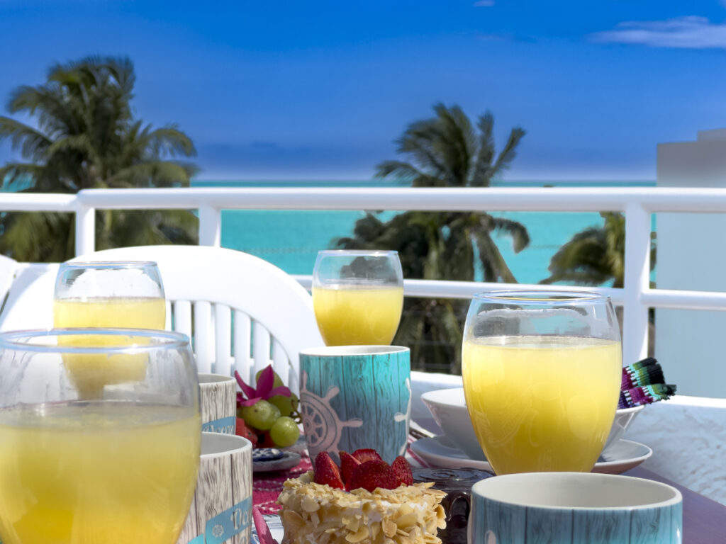 Glasses of orange juice and breakfast dishes on a rooftop table with palms and sea beyond.