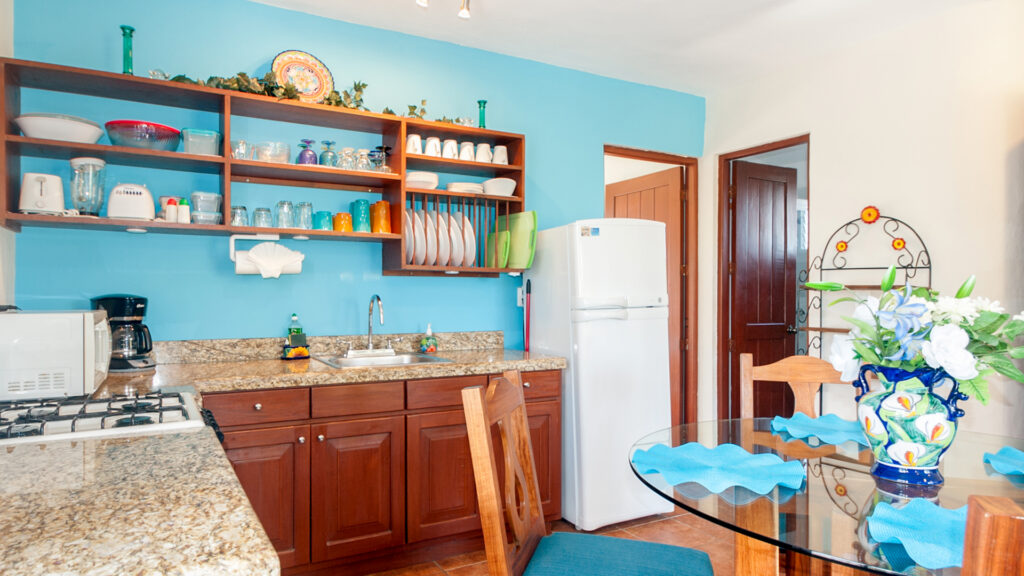 Kitchen with wooden cabinets, open dish shelves, stove, and white refrigerator against a turquoise wall.