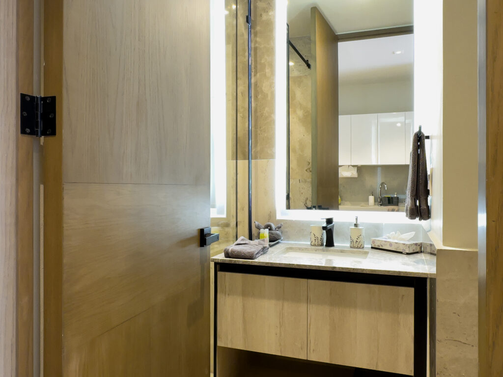 Bathroom vanity with a stone counter beneath a tall illuminated mirror.