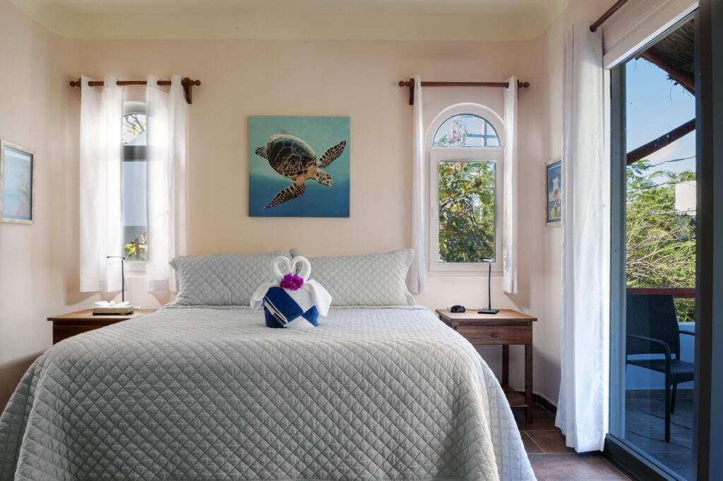 Bed with folded towel swans beneath turtle artwork between narrow arched windows.