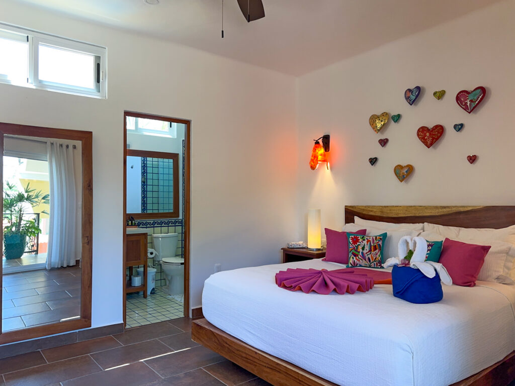 Bed beneath heart decorations beside an open bathroom doorway and tall mirror.