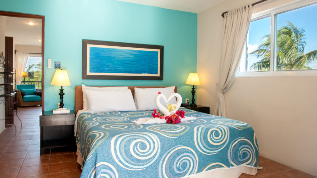 Bed with a blue spiral-patterned cover and towel swans beneath blue artwork and matching lamps.