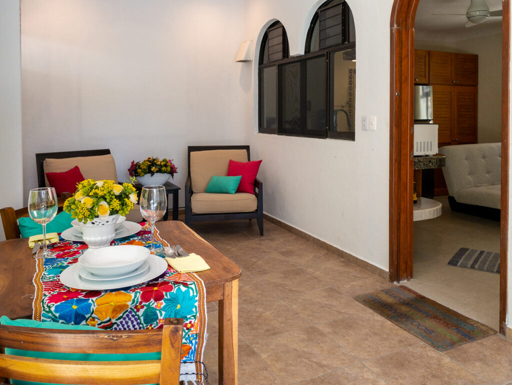 Patio table with a colorful runner and place settings beside two cushioned armchairs.