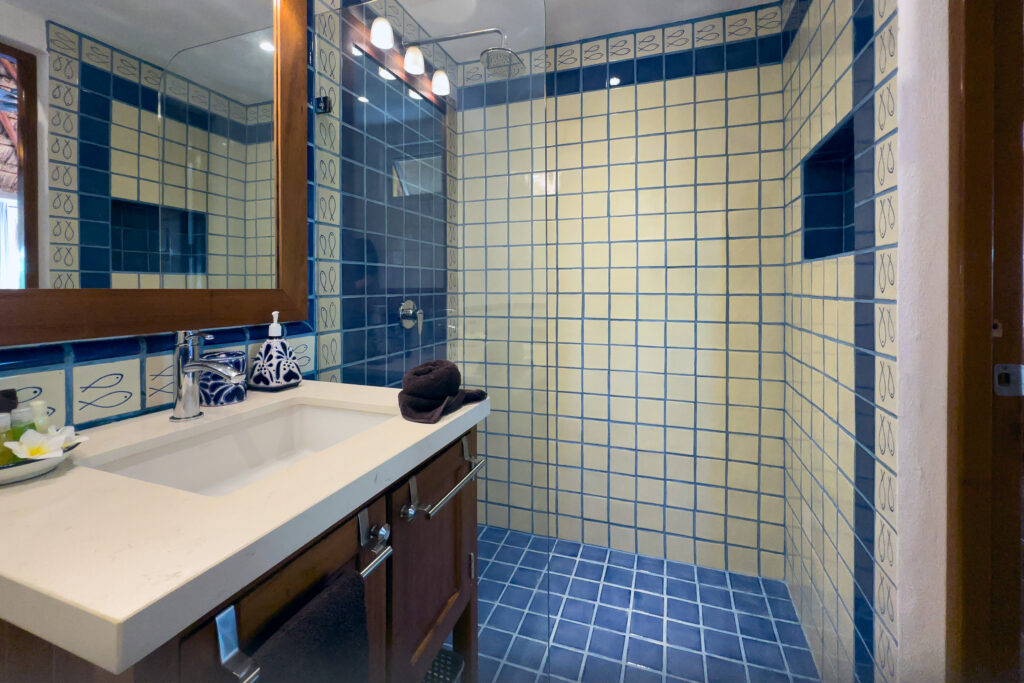 Rectangular sink and mirror beside a shower lined with blue-and-white tiles.