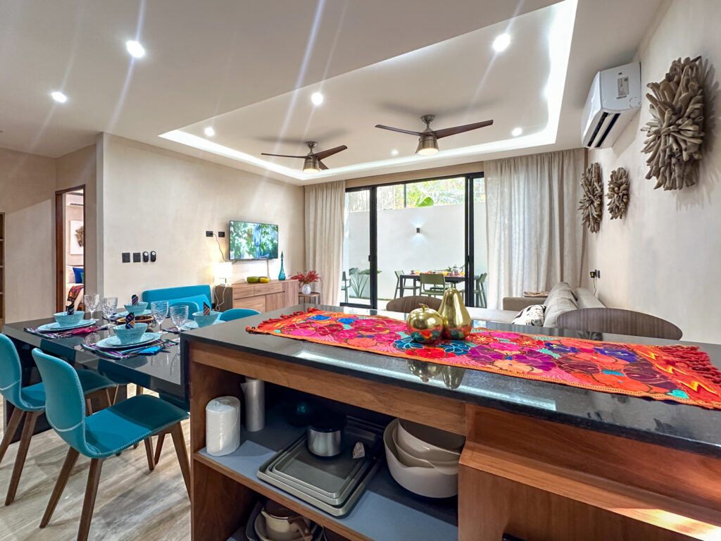Kitchen counter with a colorful runner overlooks the dining table and lounge beneath two ceiling fans.