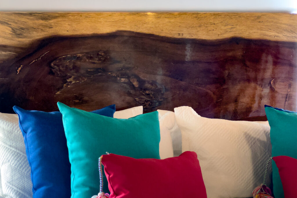 Close view of a natural wood headboard above white bedding and colorful pillows.