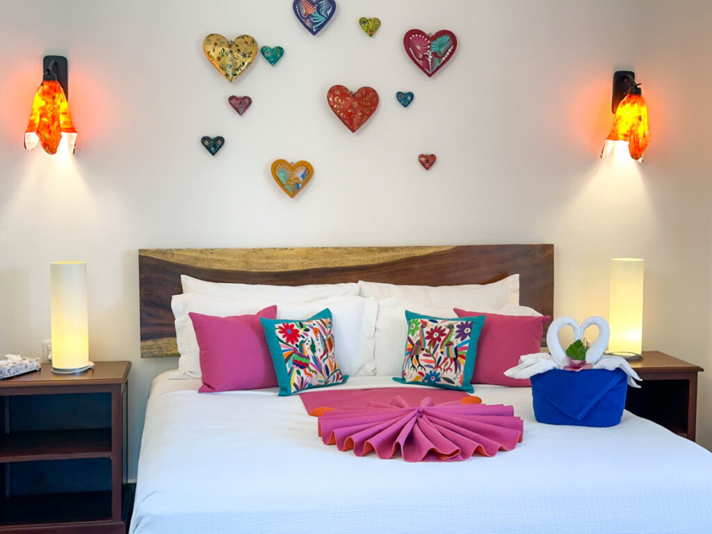 White bedding, patterned cushions, and towel swans beneath heart-shaped wall decorations.