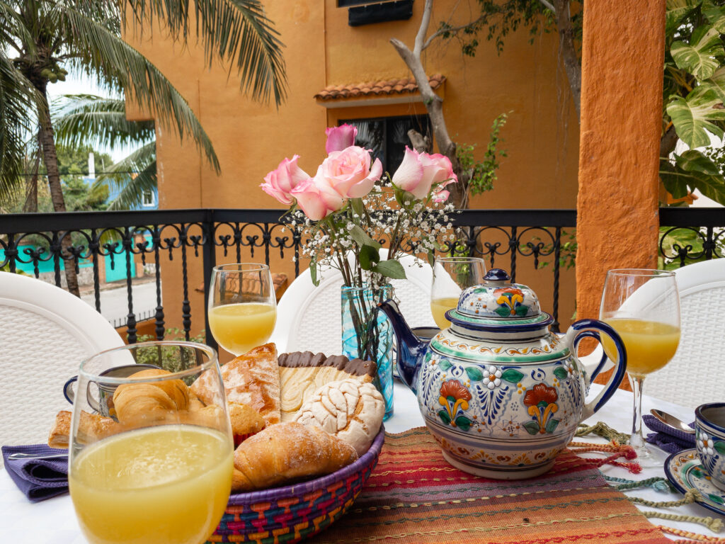 Pastries, juice, flowers, and colorful ceramic dishes arranged on a balcony table.