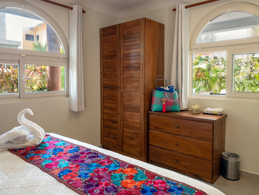 Wooden wardrobe and dresser between arched windows beside the bed.