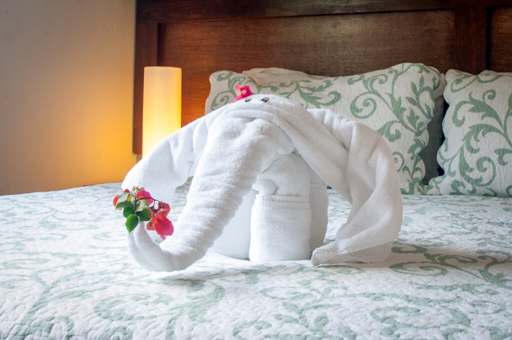 White towel folded into an elephant shape with flowers on a patterned bedspread.