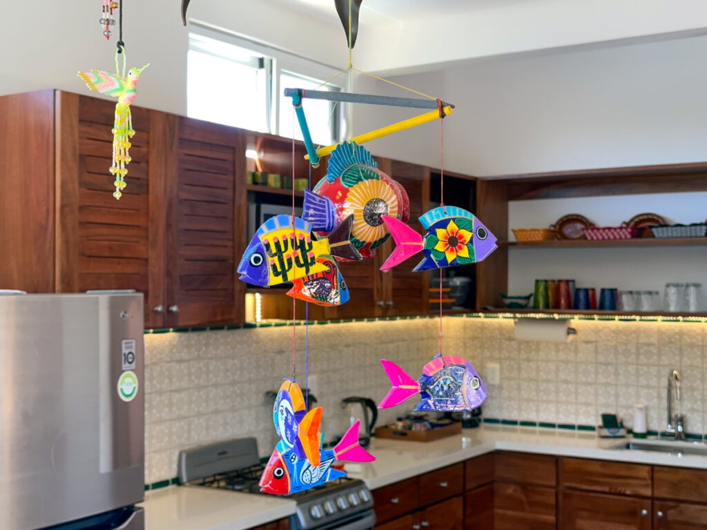 Brightly painted hanging fish above a kitchen with wooden cabinets and open shelves.